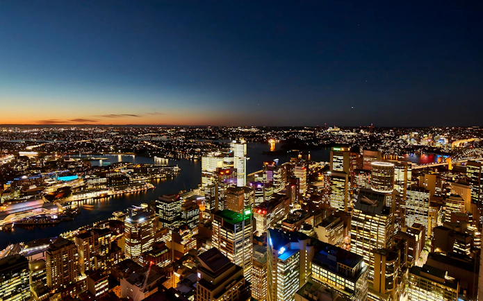 Sydney cityscape at dusk viewed from SkyFeast at Sydney Tower, with illuminated buildings and harbor.