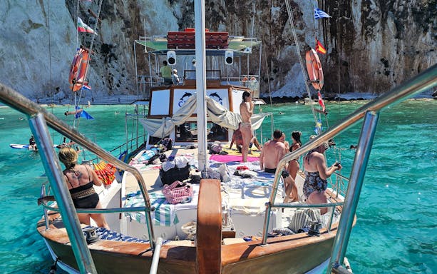 Cruise ship deck with people sunbathing and swimming in turquoise waters near Kefalonia cliffs.
