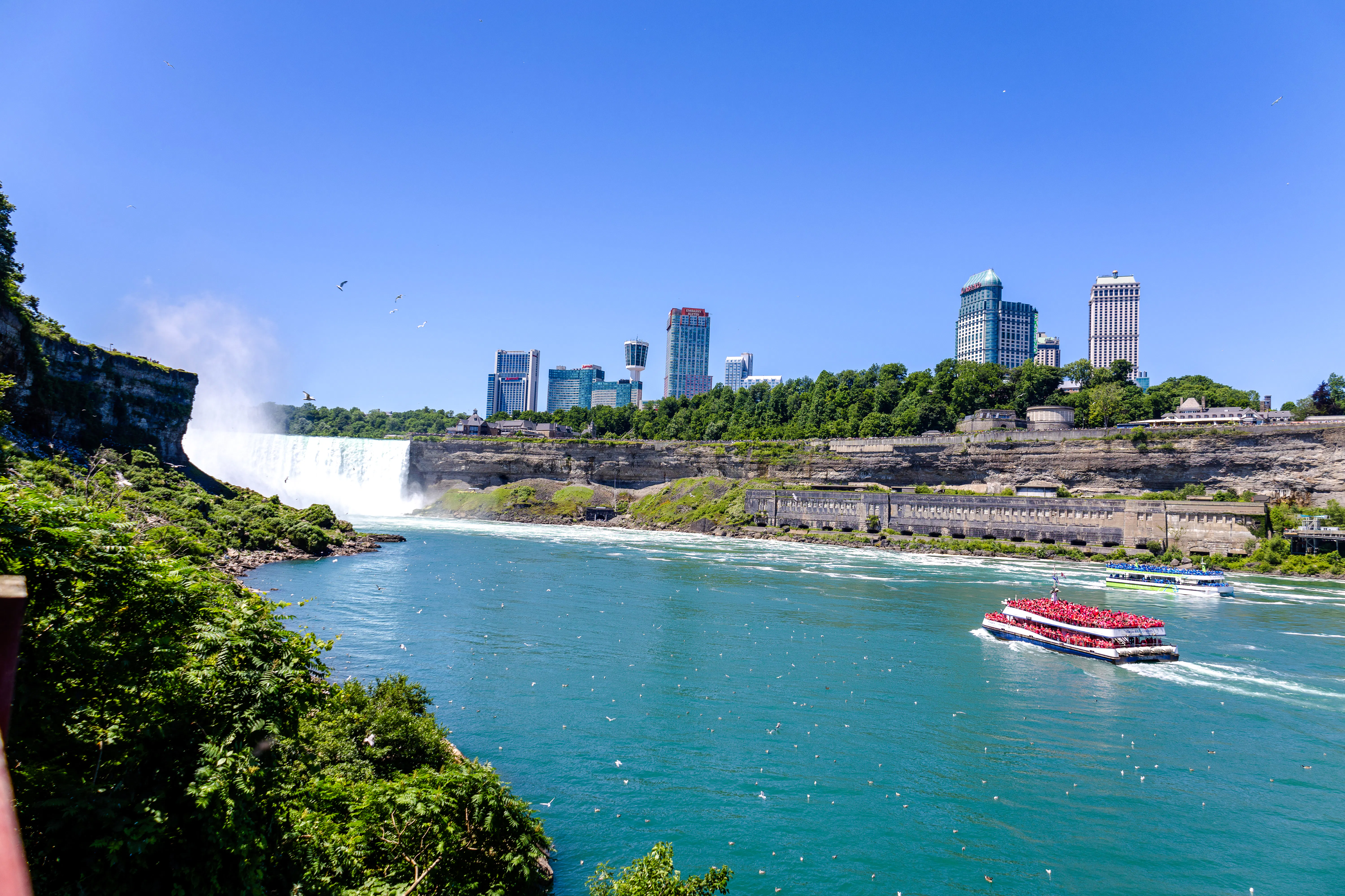Niagara Falls with tour boat on river, city skyline in background, USA.