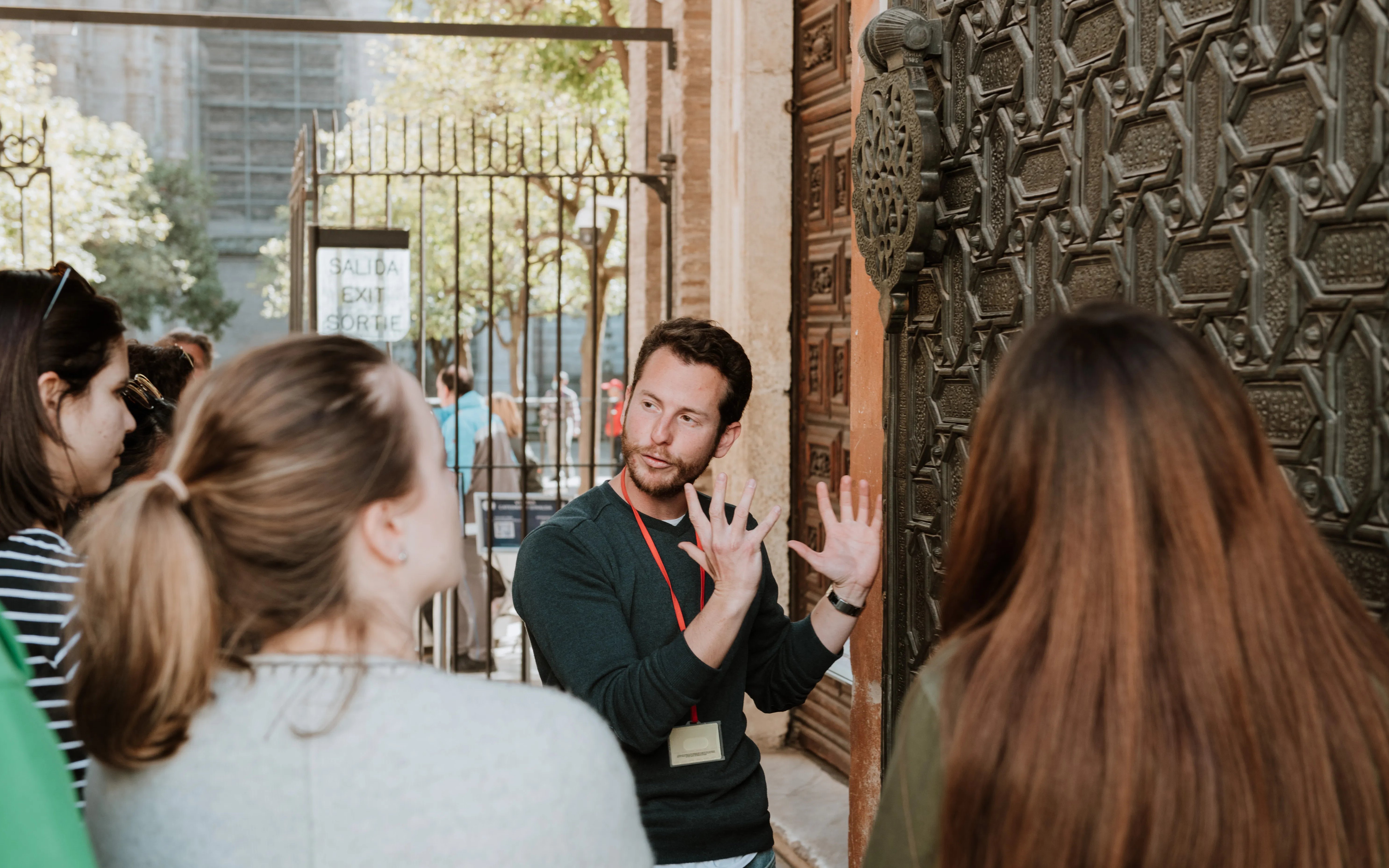 Tour guide explaining details to a group near a historic door in Seville.