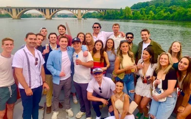 Group enjoying Boomerang Pirate Ship 21+ Party Cruise with drinks, DC monuments in background.