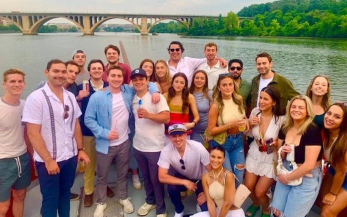Group enjoying Boomerang Pirate Ship 21+ Party Cruise with drinks, DC monuments in background.