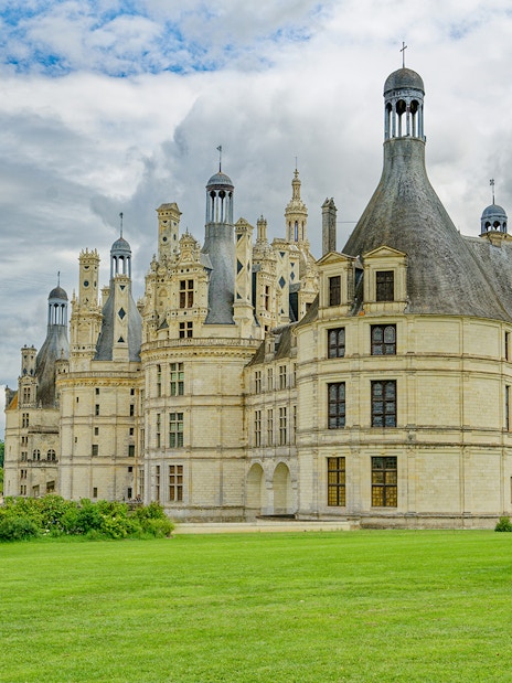 Château de Chambord with lush green grounds under a cloudy sky, part of Chambord and Chenonceau Tour.