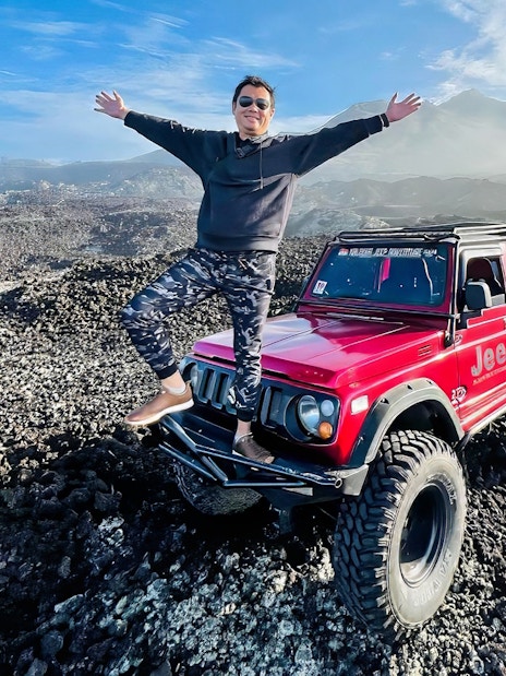 Man standing on a red jeep on rocky terrain at Mount Batur, Bali.