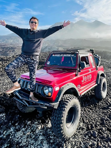 Man standing on a red jeep on rocky terrain at Mount Batur, Bali.