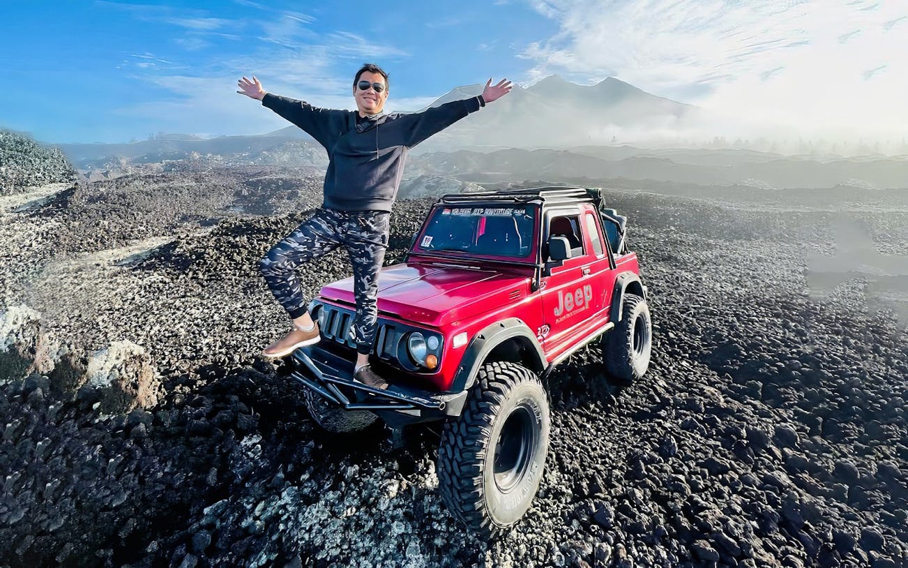 Man standing on a red jeep on rocky terrain at Mount Batur, Bali.