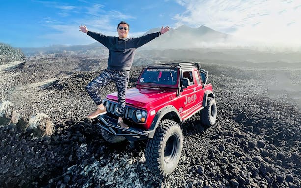 Man standing on a red jeep on rocky terrain at Mount Batur, Bali.