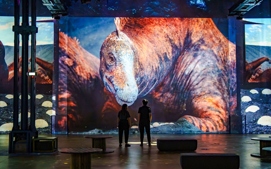 Visitors viewing dinosaur projection at Prehistoric Planet exhibition, Atelier des Lumières, Paris.
