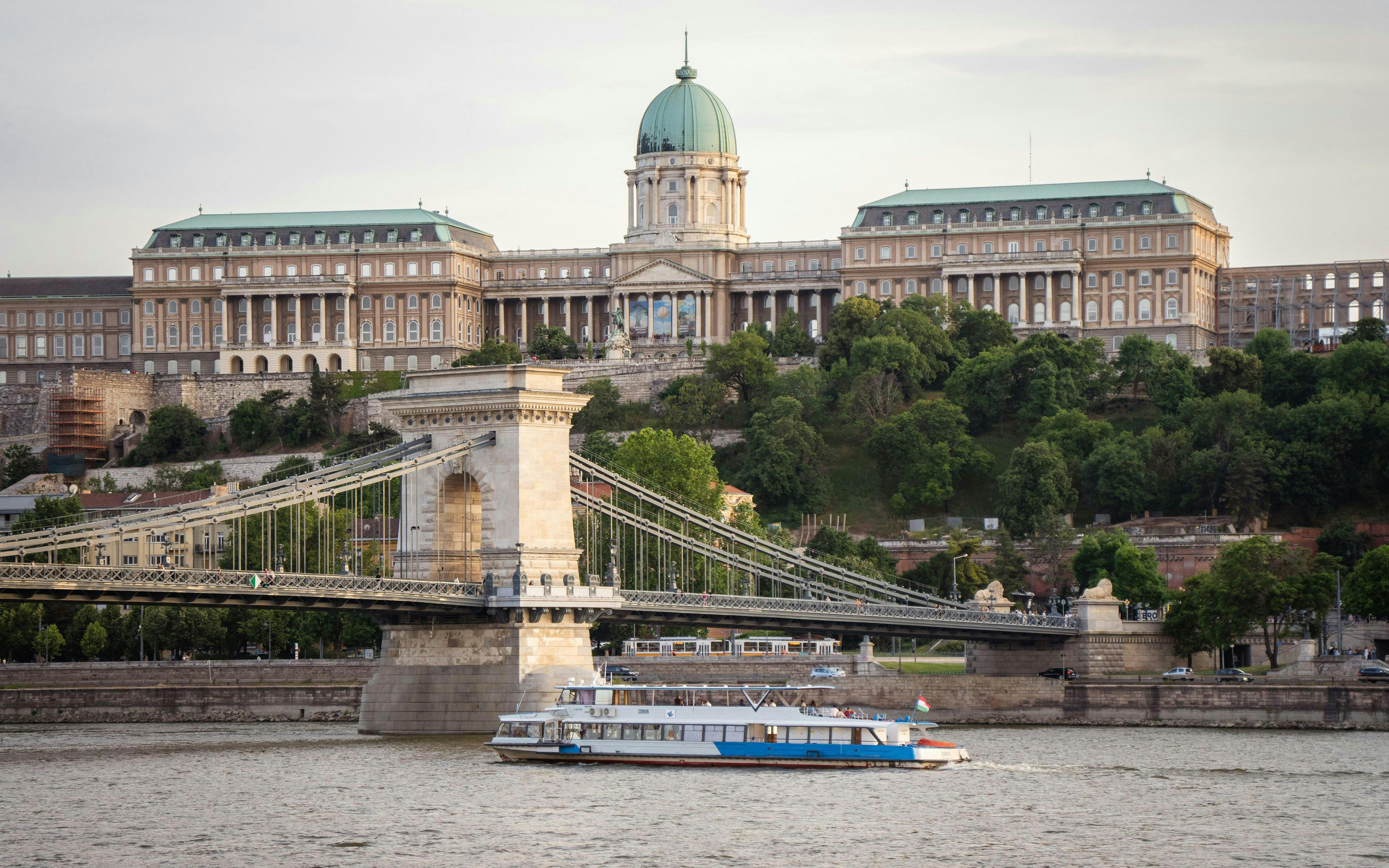 Budapest cruise boat passing Chain Bridge with Buda Castle in the background.