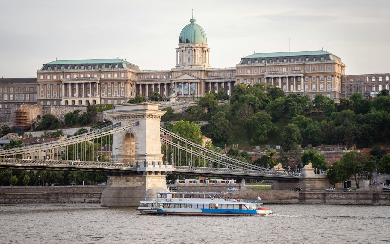 Budapest cruise boat passing Chain Bridge with Buda Castle in the background.