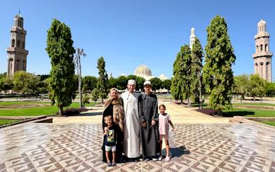 Family at Sultan Qaboos Grand Mosque gardens, Muscat, with minarets and dome in view.