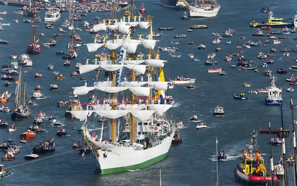 Tall ship surrounded by boats during SAIL Amsterdam event.