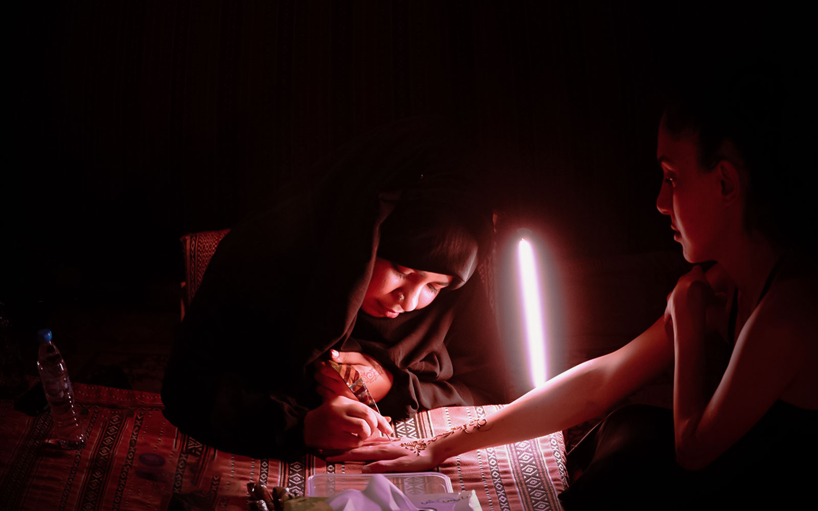 Henna artist applying design on woman's hand at Abu Dhabi desert safari.