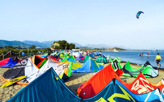 Kiteboarding setup on the beach at Delta Neretva, Croatia with colorful kites and distant mountains.