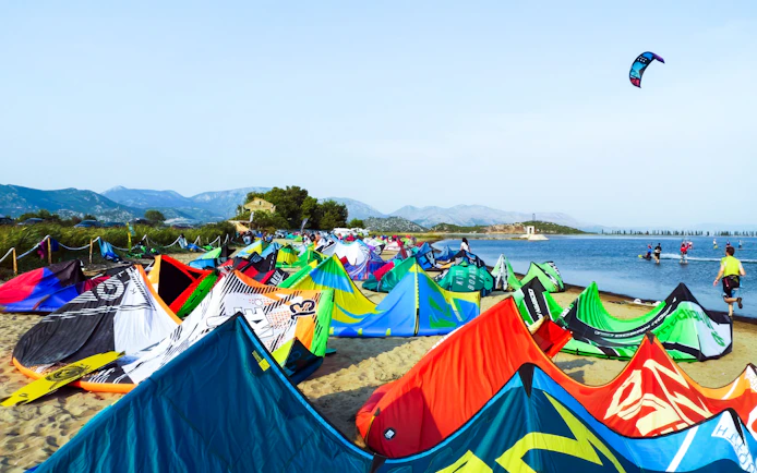 Kiteboarding setup on the beach at Delta Neretva, Croatia with colorful kites and distant mountains.