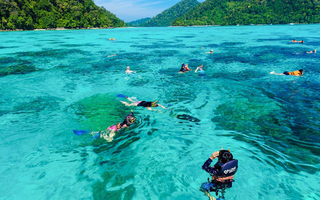 Tourists snorkeling in clear turquoise waters of Surin Islands, Thailand.