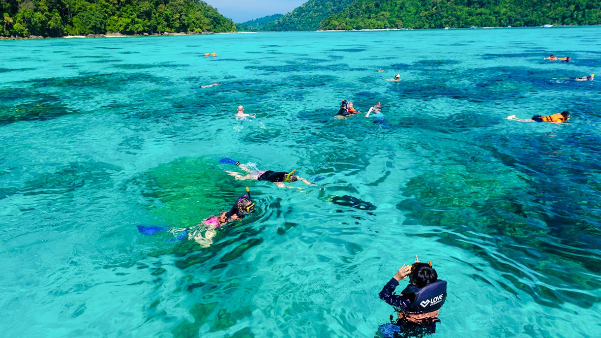 Tourists snorkeling in clear turquoise waters of Surin Islands, Thailand.