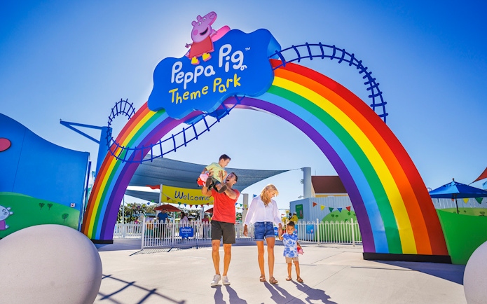 Family entering Peppa Pig Theme Park under rainbow arch, Florida.