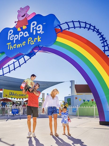 Family entering Peppa Pig Theme Park under rainbow arch, Florida.