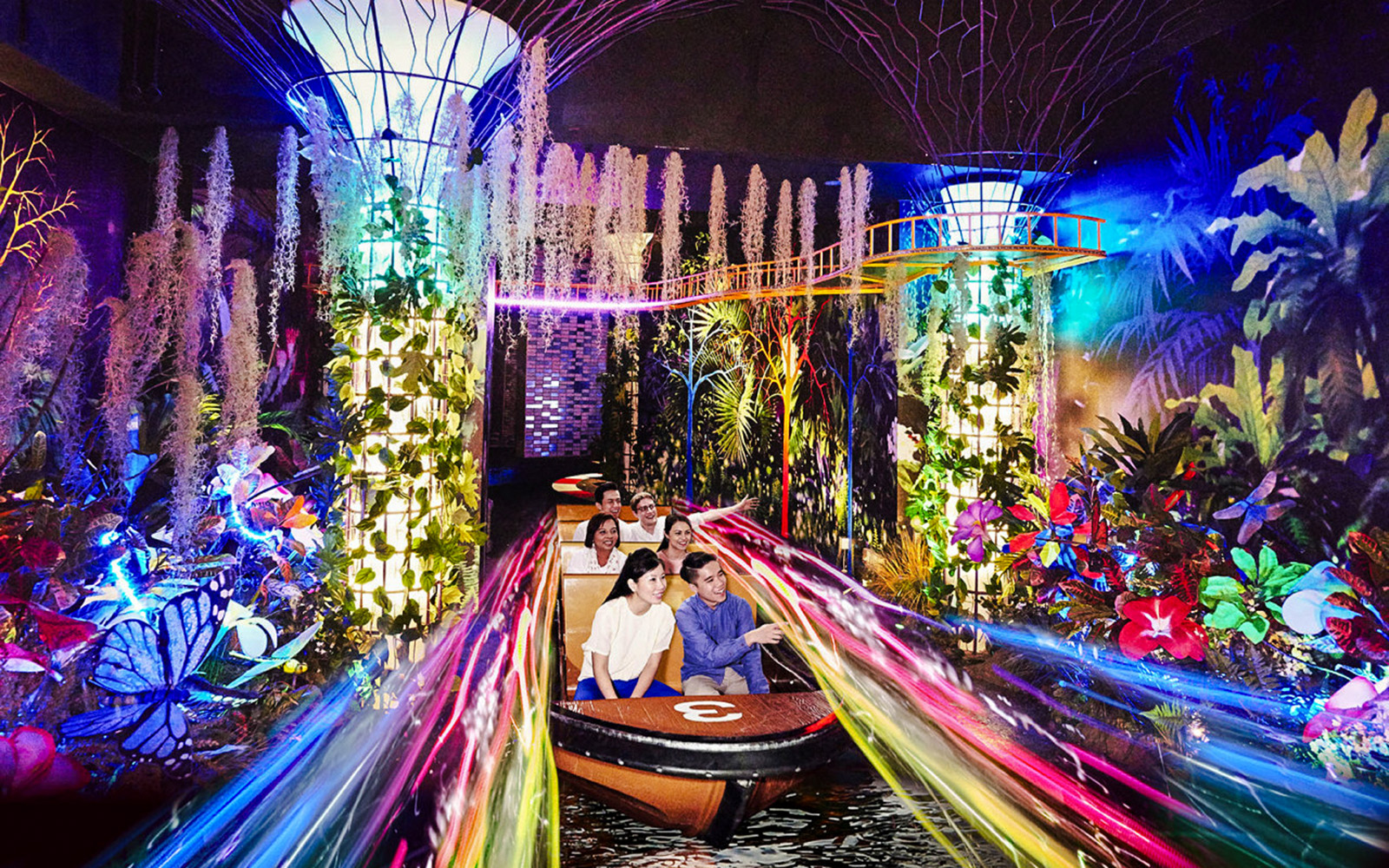 Visitors on a boat ride through vibrant, illuminated gardens at Madame Tussauds Singapore.