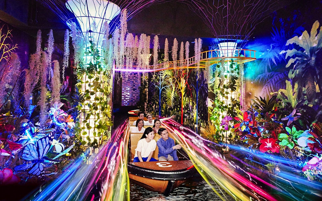 Visitors on a boat ride through vibrant, illuminated gardens at Madame Tussauds Singapore.