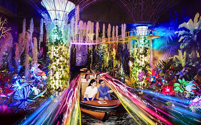 Visitors on a boat ride through vibrant, illuminated gardens at Madame Tussauds Singapore.