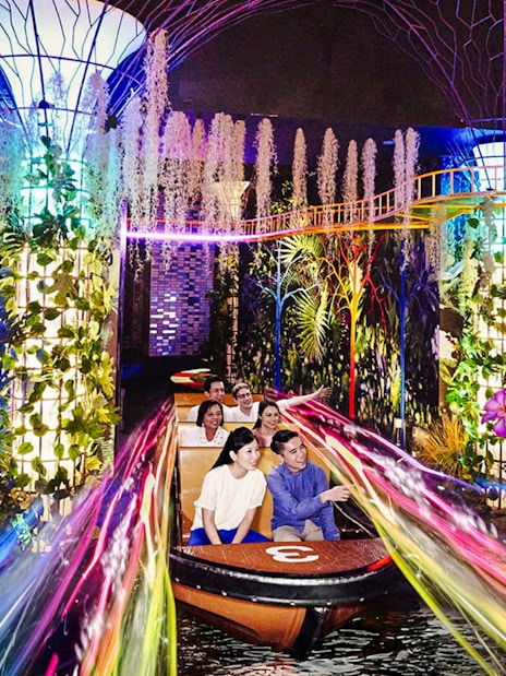 Visitors on a boat ride through vibrant, illuminated gardens at Madame Tussauds Singapore.