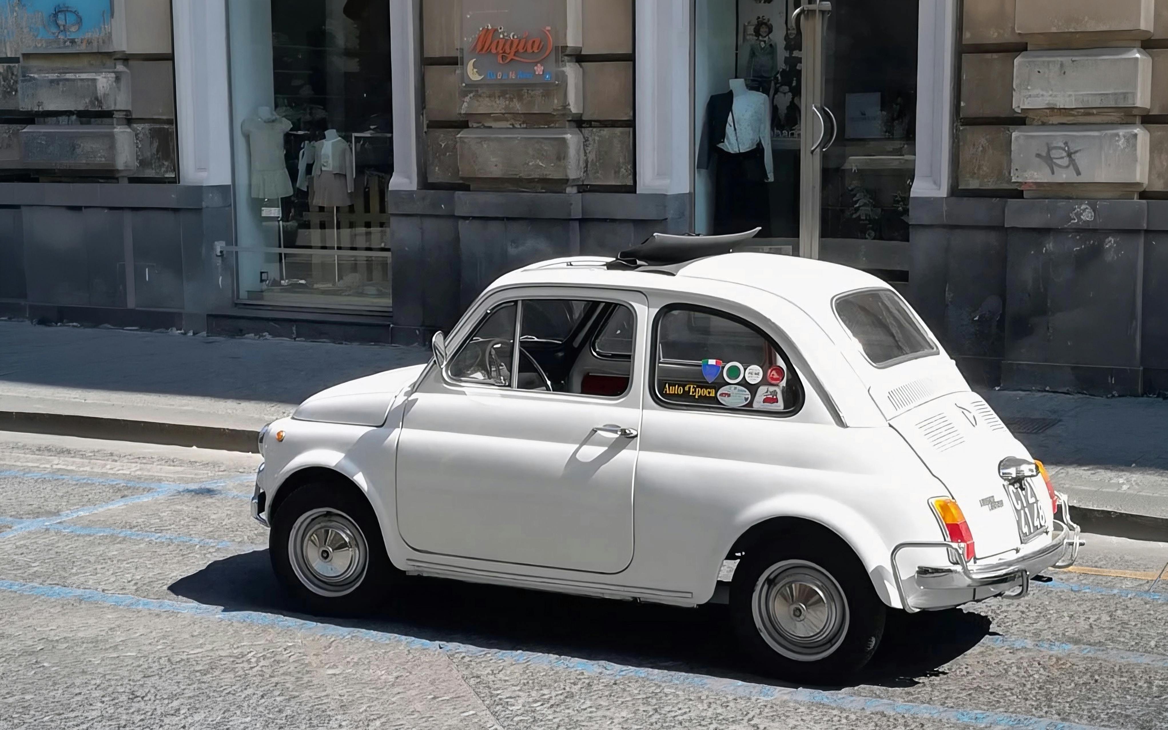 Fiat 500 parked on a city street near a clothing store.