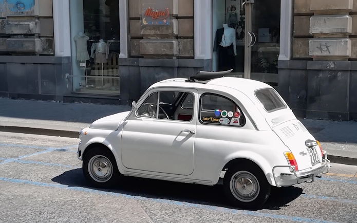 Fiat 500 parked on a city street near a clothing store.