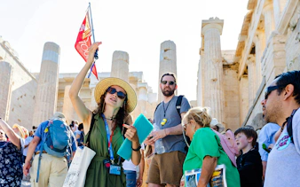 Tour guide leading a group at the Acropolis with Parthenon in the background, Athens.