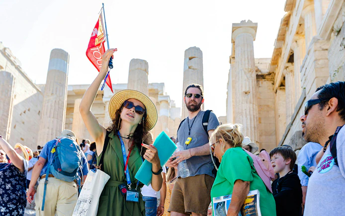 Tour guide leading a group at the Acropolis with Parthenon in the background, Athens.