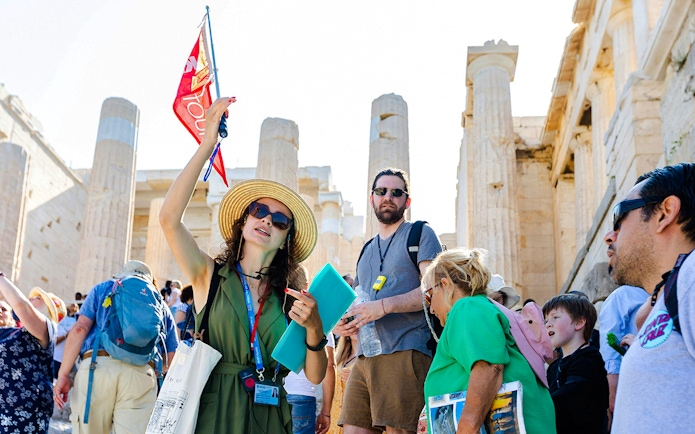 Tour guide leading a group at the Acropolis with Parthenon in the background, Athens.