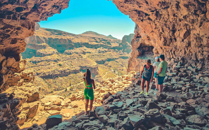 Tourists exploring rocky cave with view of Red Canyon, Gran Canaria.
