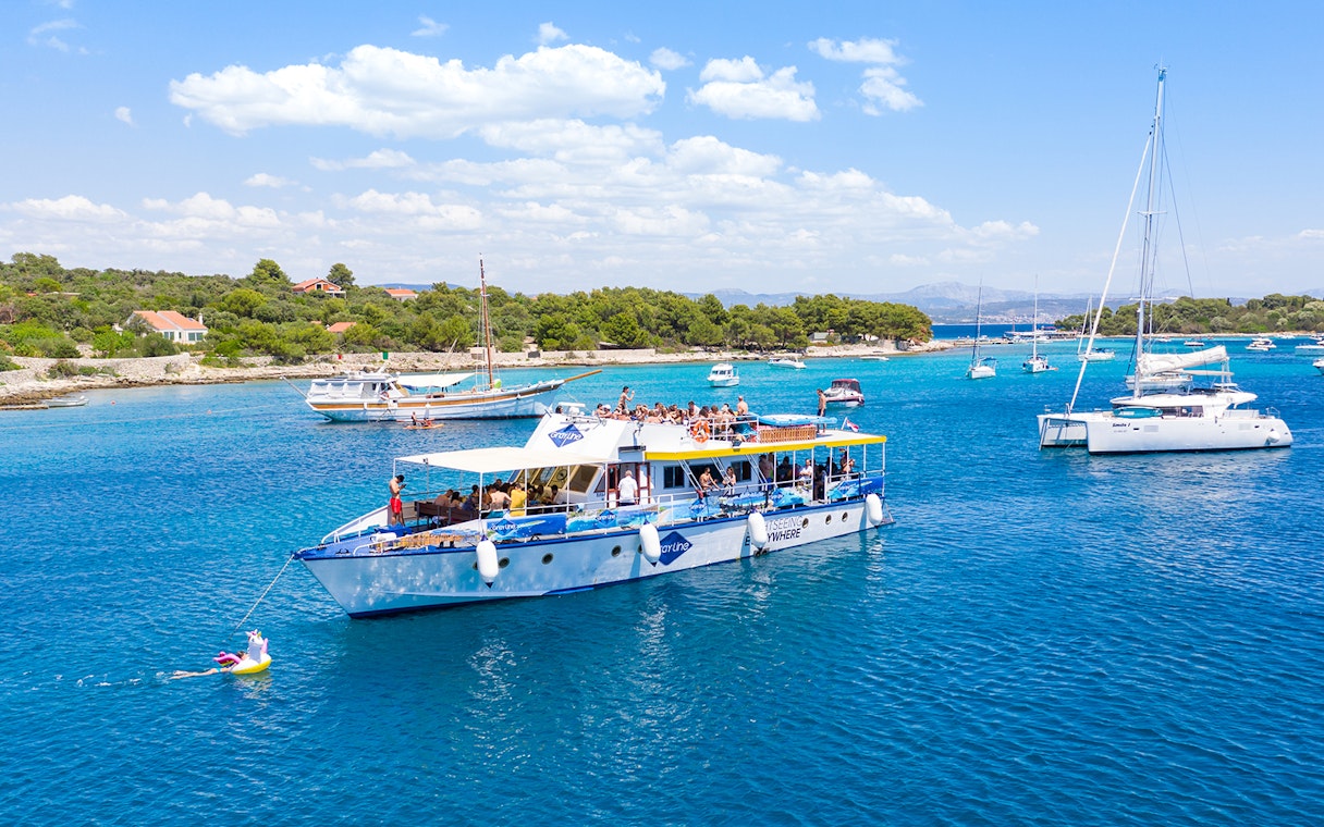 Cruise ship with tourists in Split's Blue Lagoon, surrounded by sailboats and clear blue water.
