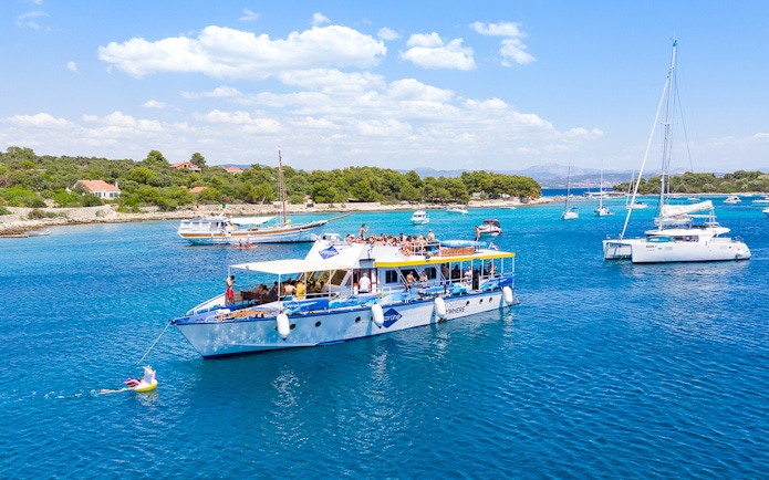 Cruise ship with tourists in Split's Blue Lagoon, surrounded by sailboats and clear blue water.
