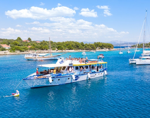 Cruise ship with tourists in Split's Blue Lagoon, surrounded by sailboats and clear blue water.