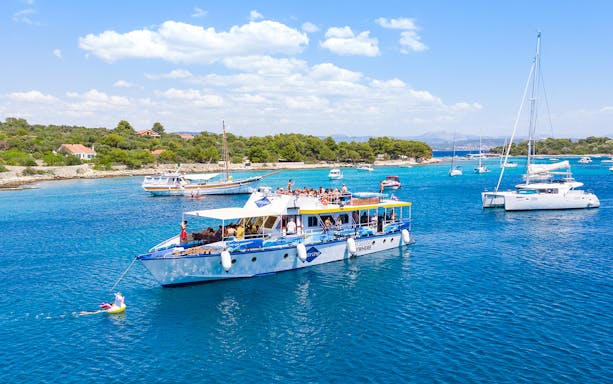 Cruise ship with tourists in Split's Blue Lagoon, surrounded by sailboats and clear blue water.