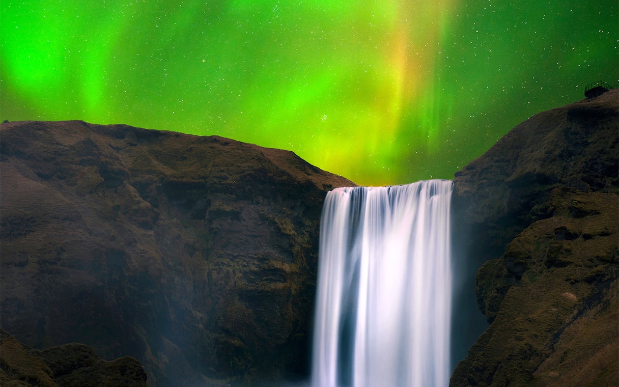 Skógafoss Waterfall in Iceland with northern lights in the sky.