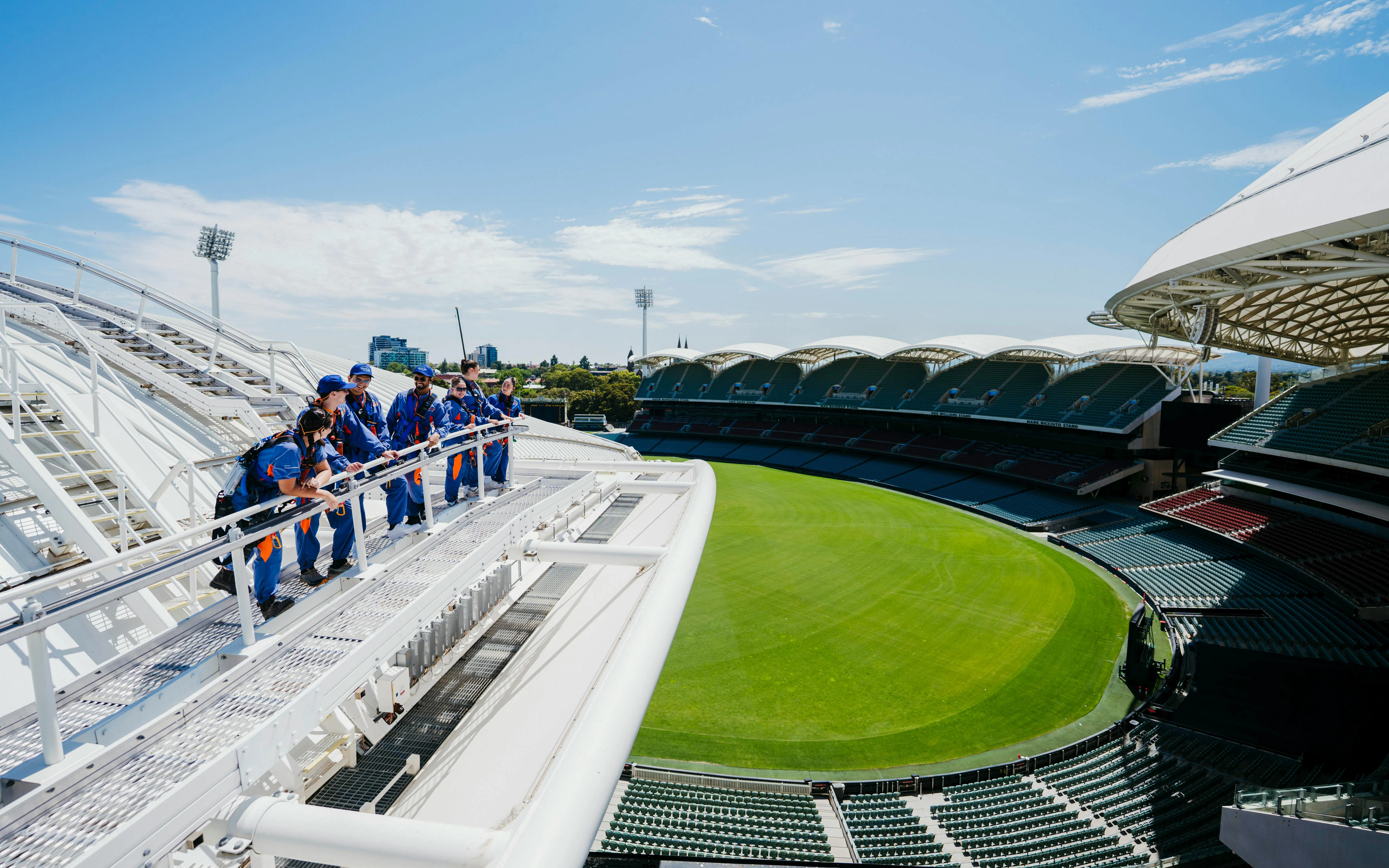 Group climbing Adelaide Oval roof with view of stadium and city skyline.