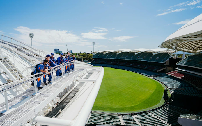 Group climbing Adelaide Oval roof with view of stadium and city skyline.