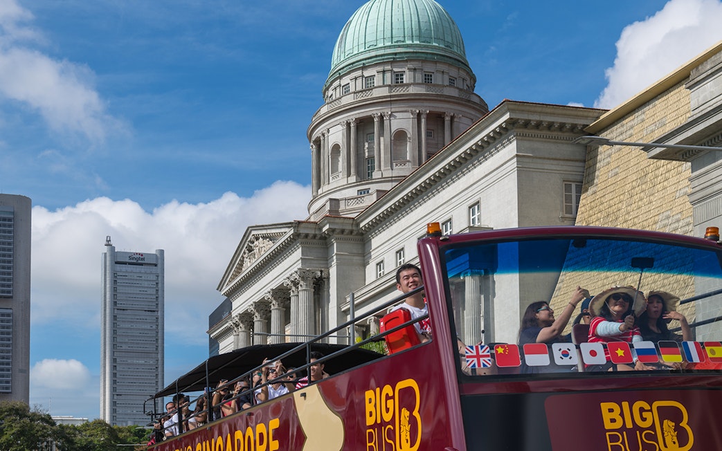 Tourists on a Singapore hop-on-hop-off bus tour with historic architecture in the background.