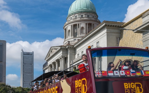 Tourists on a Singapore hop-on-hop-off bus tour with historic architecture in the background.