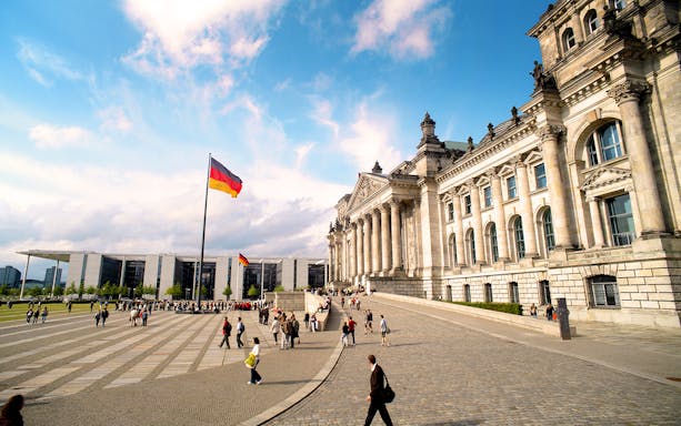 Reichstag building with German flags and tourists in Berlin's Parliament District.
