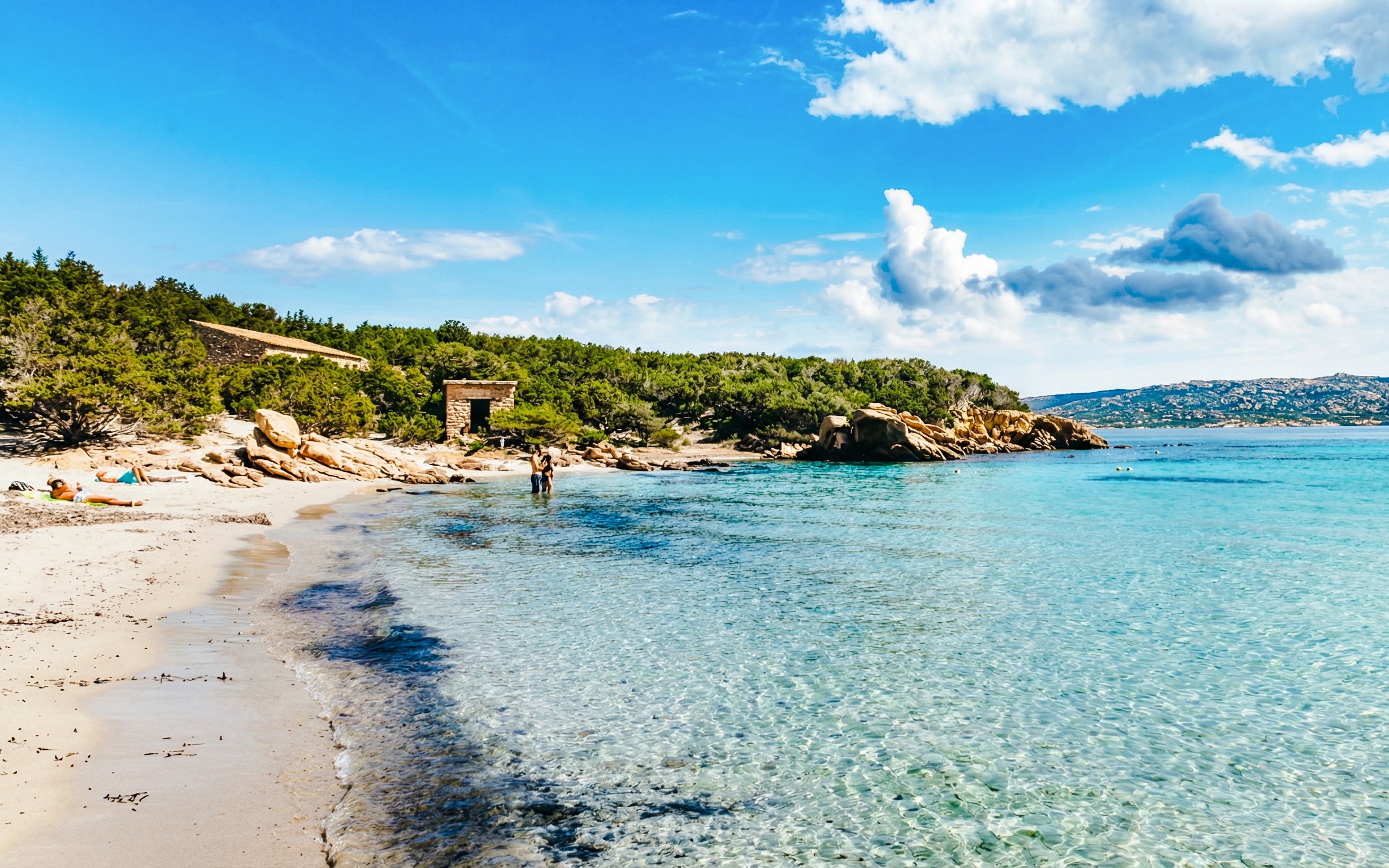 La Maddalena Archipelago beach with clear water and rocky shoreline on a sunny day.