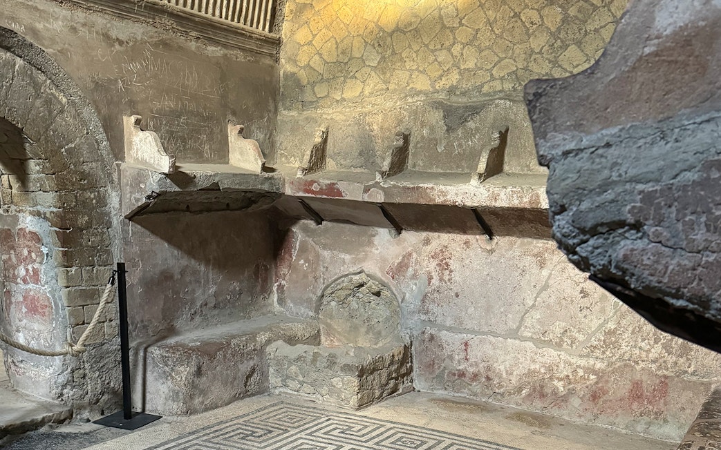 Herculaneum Ruins ancient bathhouse interior with stone seating and mosaic floor.