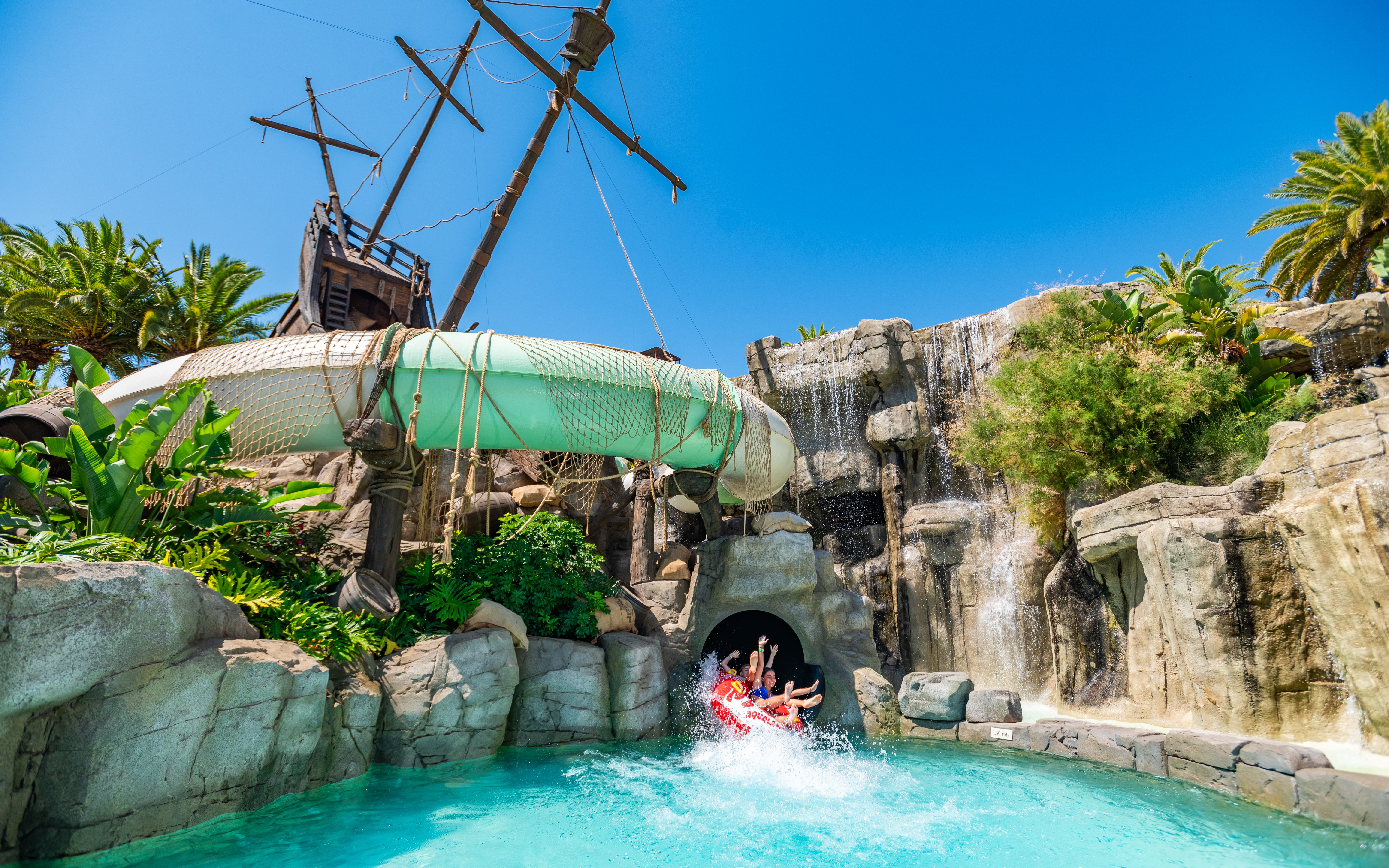 Visitors on water slide at Aqualand Torremolinos with pirate ship backdrop.