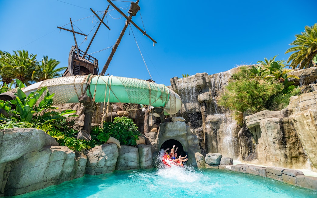 Visitors on water slide at Aqualand Torremolinos with pirate ship backdrop.