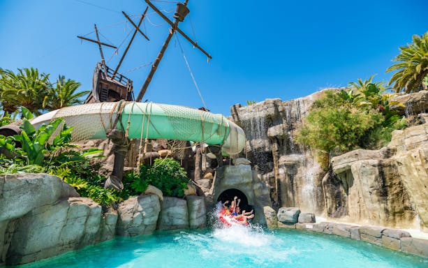 Visitors on water slide at Aqualand Torremolinos with pirate ship backdrop.