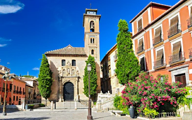 Historic church facade in Albaicin, Granada, with bell tower and vibrant flowers.
