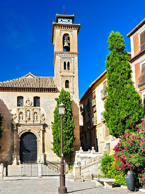 Historic church facade in Albaicin, Granada, with bell tower and vibrant flowers.